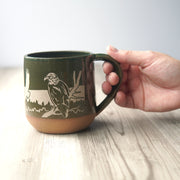 Bald Eagles engraved handmade pottery mug in pine green, shown with a hand holding it