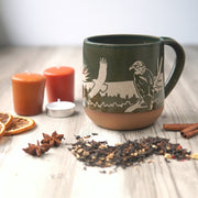 Bald Eagles engraved handmade pottery mug in pine green, shown with fall candles, spices, and chai tea