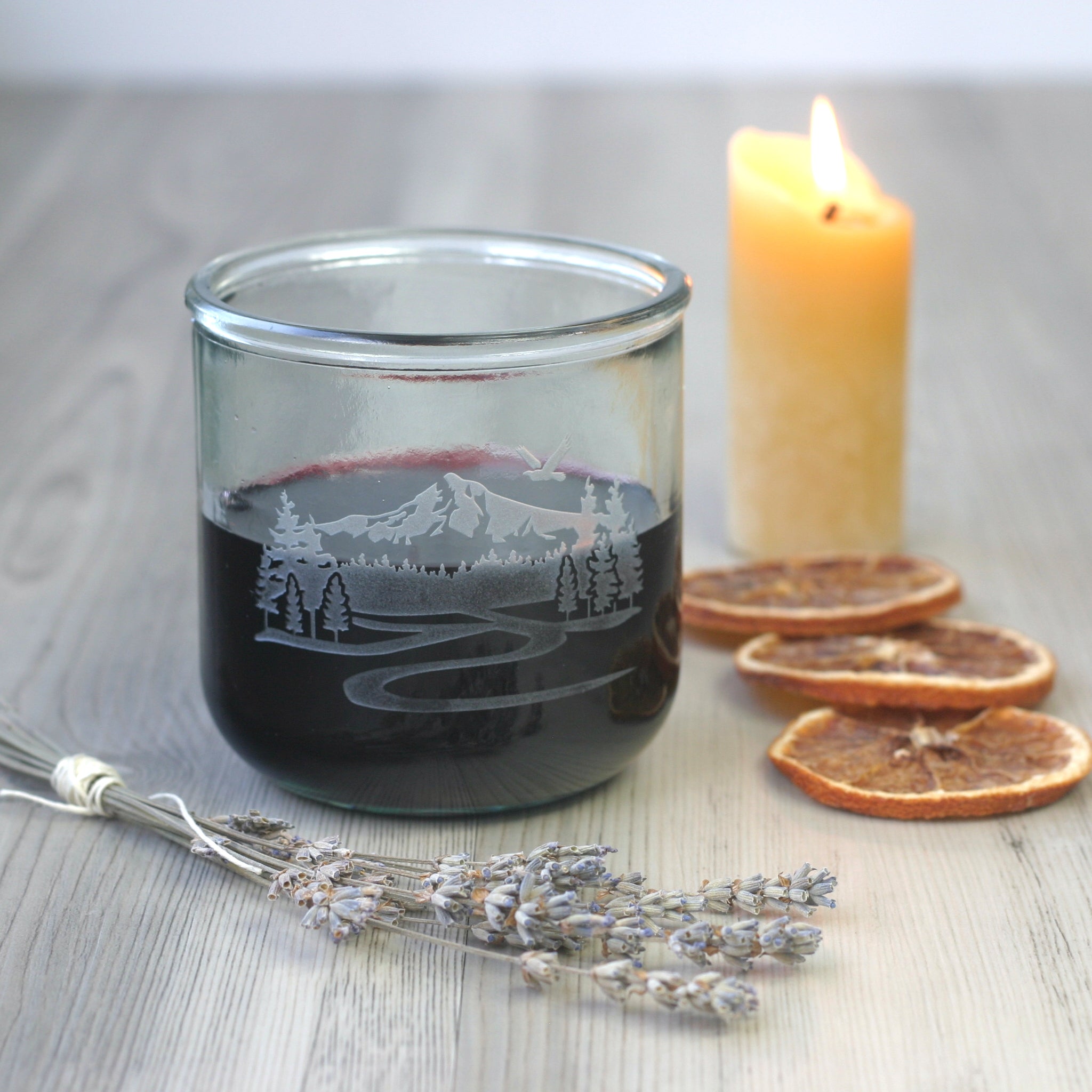 Mt Hood short glass with red wine, beside lavender bundle, orange slices, and lit beeswax candle